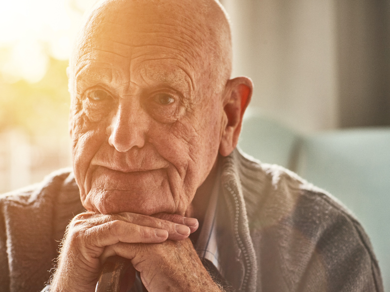 An older man looks sad, resting his chin on the back of his hands.